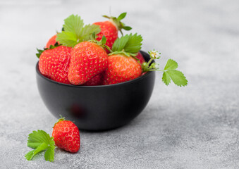 Organic fresh raw strawberries with leaf in black ceramic bowl on light background.