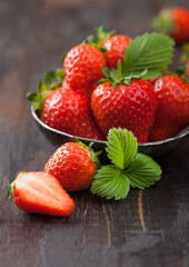 Fresh raw organic strawberries with leaf in steel bowl on wooden background.