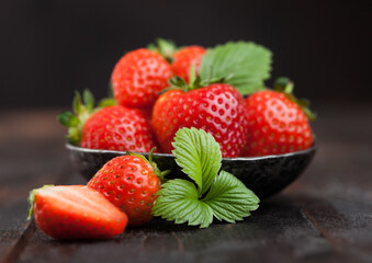 Fresh raw organic strawberries with leaf in steel bowl on wooden background.