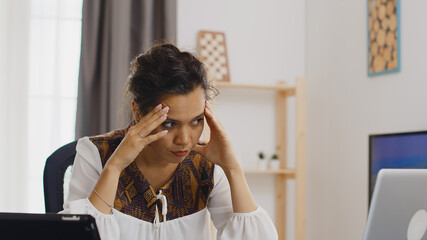 Tired woman in home office looking at laptop during quarantine.