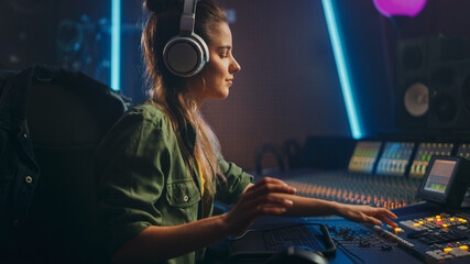 Portrait of Beautiful Female Artist Musician in Music Recording Studio, Uses Headphones.  Successful Female Audio Engineer Uses Mixing Board Create Modern Song.