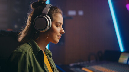 Portrait of Beautiful Female Artist Musician in Music Recording Studio Uses Headphones, Mixing...