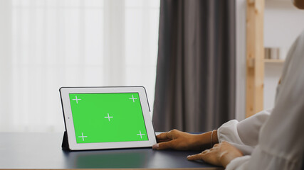 Woman using tablet computer with green screen in home office.