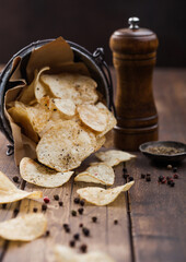 Potato crisps chips snack with black pepper in steel  bucket on wooden background with mill and ground pepper.