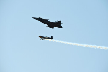 Two planes performing stunts and spectacular maneuvers in the air, white smoke, blue sky in the...
