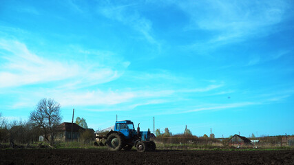 Fototapeta premium The tractor cultivates and cuts furrows in the field. Tractor work in the black soil field in the village