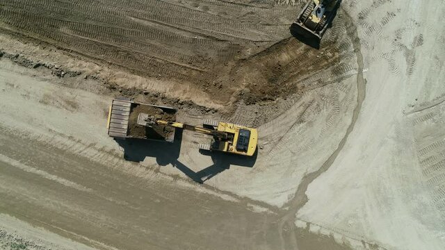 Top-Down View . An Industrial Excavator On An Open Road Section Loads Rock And Earth On A Very Large Dump Truck, A Bulldozer Rakes The Earth .The Excavator Is Working .Unmanned Image Of A Construction
