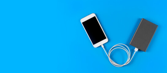 Top view smartphone charging with power bank on blue background with copy space. Smartphone charging with power bank by white USB cable.