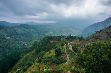 View from above to the green mountains, pathway, smoke, grey clouds and village in Sri Lanka.