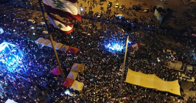 Beirut, Lebanon 2019 : night drone shot passing by the Lebanese flag and stages in Martyr square, during the Lebanese revolution, with thousands of protesters revolting against government failure 