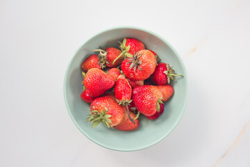 Strawberries in a green ceramic plate on a white marble table. Card with copy space for text. Top view, flatlay
