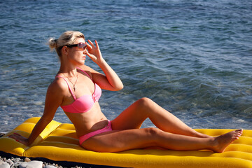 Happy woman in sunglasses sitting on air mattress by the sea