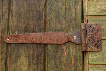 An old rusty exterior door hinge holds a green door, sometimes blackened.
