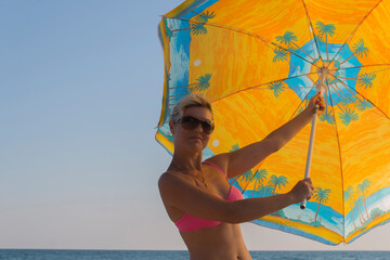 Smiling woman in sunglasses against a blue sky holds a large parasol in his hands