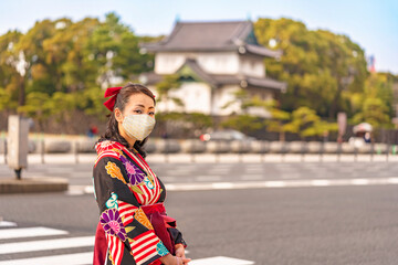 Japanese woman in hakama kimono in front of the dungeon Edojō sakurada tatsumiyagura with moats lined with pine trees outside of the Tokyo Imperial Palace.