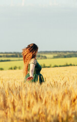 Beautiful woman in green dress with flying long hair, girl walking in field of wheat, girl enjoying summer nature, freedom concept