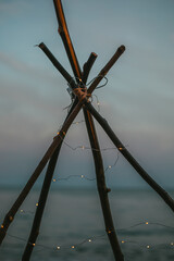 Fototapeta premium Branches teepee with little lanterns on the beach