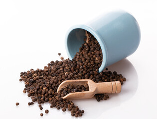black pepper in a clay pot with a wooden spoon, isolated on a white background