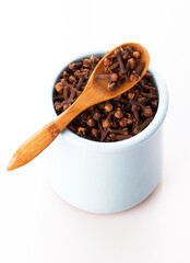 clove seasoning in a clay pot with a wooden spoon close up isolated on a white background