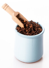 clove seasoning in a clay pot with a wooden spoon close up isolated on a white background