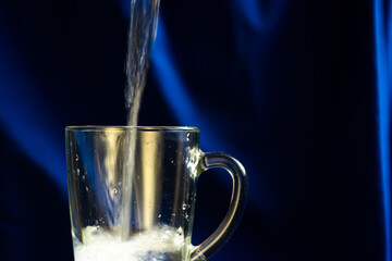 Water pours into a transparent mug on a blue background