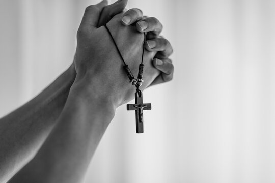 Christian male hands praying while firmly holding a rosary with a cross at church.