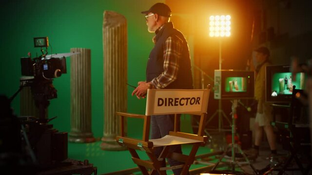 Prominent Successful Senior Director Takes Place at His Chair and Commands "Action!" to Start Shooting. On the Studio Film Set with High End Equipment Professional Crew Shooting High Budget Movie