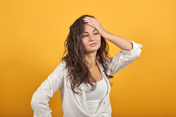 Stress or a headache grimacing in pain holds the back of neck indicating location. Fatigue during workaholism labor. Young attractive woman, dressed white blouse, with brown eyes, curly hair, yellow