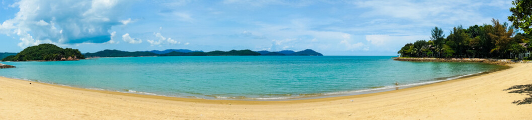 Fototapeta na wymiar Panoramic shot of a beautiful golden sand beach with blue water beautiful fluffy clouds shot in Malaysia