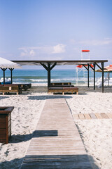 beach with wooden arbors, white umbrellas and a path

