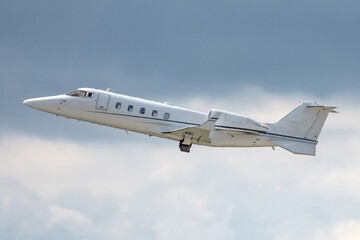 Side view of business jet airplane after taking off on grey white clouds in blue sky background. Fast modern aircraft for air transportation. Aviation technology. Travel and business concept.