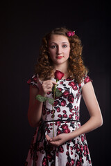 Fototapeta premium Cute girl in pin-up style with a red rose in hand, posing in Studio on red paper background. Stylish photography in vintage style.