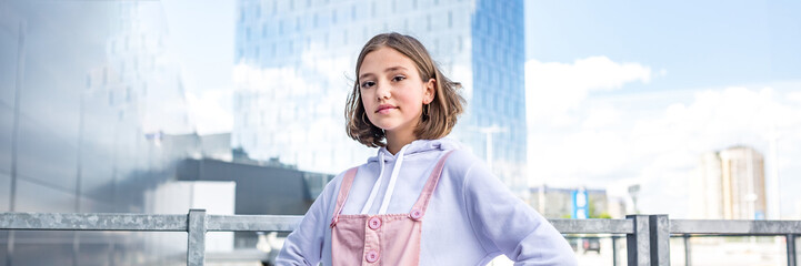 young blonde schoolgirl in a pink dress and sunglasses posing in the parking. panoramic view