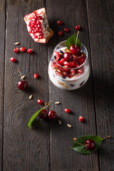 Healthy breakfast in a glass with fresh fruits: pomegranate, cherry, nectarines, honeysuckle, yogurt and granola on a black background. Shallow depth of field with selective focus 