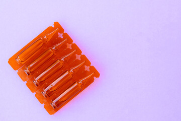 Ampoules with medication for injection on the corner of purple bacground. Transparent capsules with liquid drug for health care. Pharmaceutical industry.