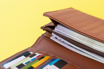Brown wallet full of credit and discount cards and american dollar banknotes  on yellow background.Copy space