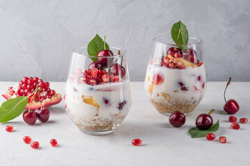 Healthy breakfast in a glass with fresh fruits: pomegranate, cherry, nectarines, honeysuckle, yogurt and granola on a grey background. Shallow depth of field with selective focus