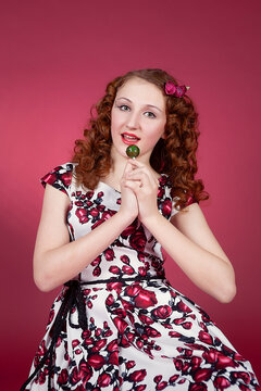 Portrait of a cute girl in pin-up style with candy in hand on red paper background. Stylish photography in vintage style.