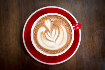 Top view of coffee in a red mug and saucer. The top surface of the coffee is shaped like a...