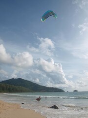 Vertical photo of kite surf sport on the beach. Wave riding. Kitesurfer goes to the water, kiteboarding parachute soars in the sky. Active moving, pulling across water surface by a power kite. 