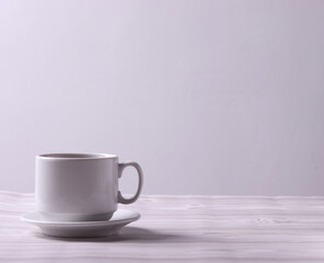 a white ceramic cup with tea or coffee and a saucer on the light background