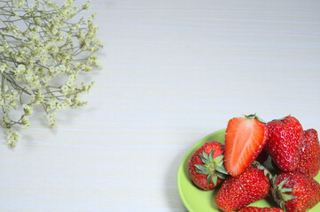 Red and juicy strawberries, red fruit and bouquet of white gypsophila on table