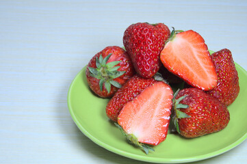 Closeup of ripe organic strawberries on green plate, whole and cut strawberries