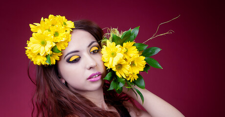Portrait of a cute girl with bright yellow makeup and yellow chrysanthemums on a red background in the Studio.