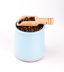 black pepper in a clay pot with a wooden spoon, isolated on a white background