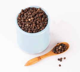 black pepper in a clay pot with a wooden spoon, isolated on a white background