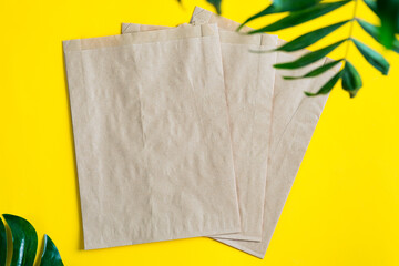 Brown mock-up craft paper bags for packaging different goods and products on a yellow background with green tropical leaves.