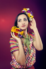 Naklejka premium Portrait of a cute girl with bright makeup and with the blooming freesias on his head and hands on a red background in the Studio.