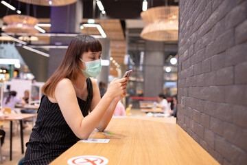 Asian woman sitting separated in restaurant eating food .keep social distance for protect infection from coronavirus covid-19, restaurant and social distancing concept.