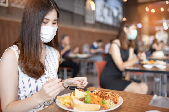 Asian woman sitting separated in restaurant eating food .keep social distance for protect infection from coronavirus covid-19, restaurant and social distancing concept.